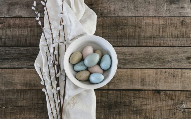 A bowl of dyed Easter eggs on a wooden table with seasonal decorations.